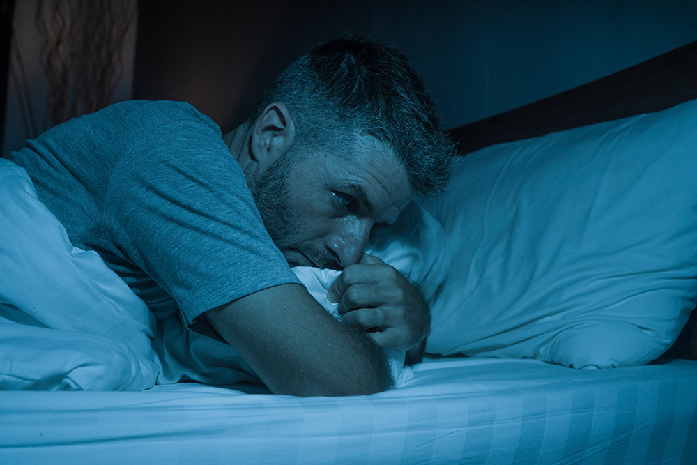 a man lying in bed at night; he is awake and looks anxious